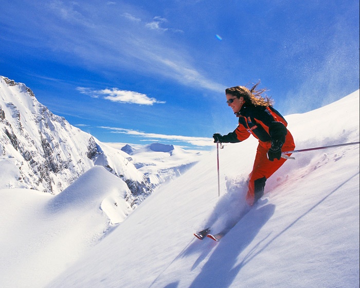 Лыжник скатывается. Девушка на лыжах в горах. Спуск с гор на лыжах. Катание на горных лыжах. Лыжник в горах.